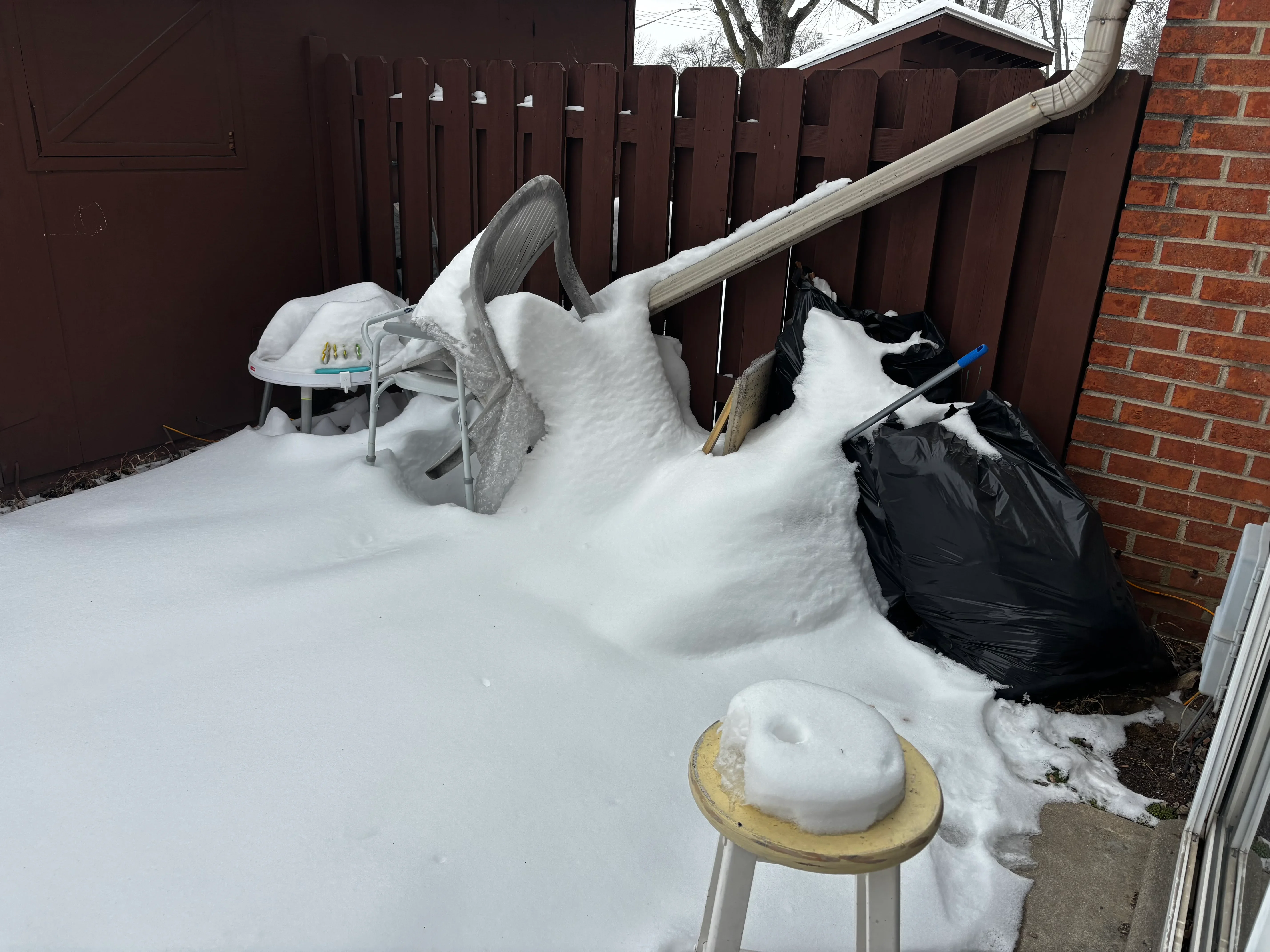 Snow-covered backyard with cleared patio area and organized debris bags