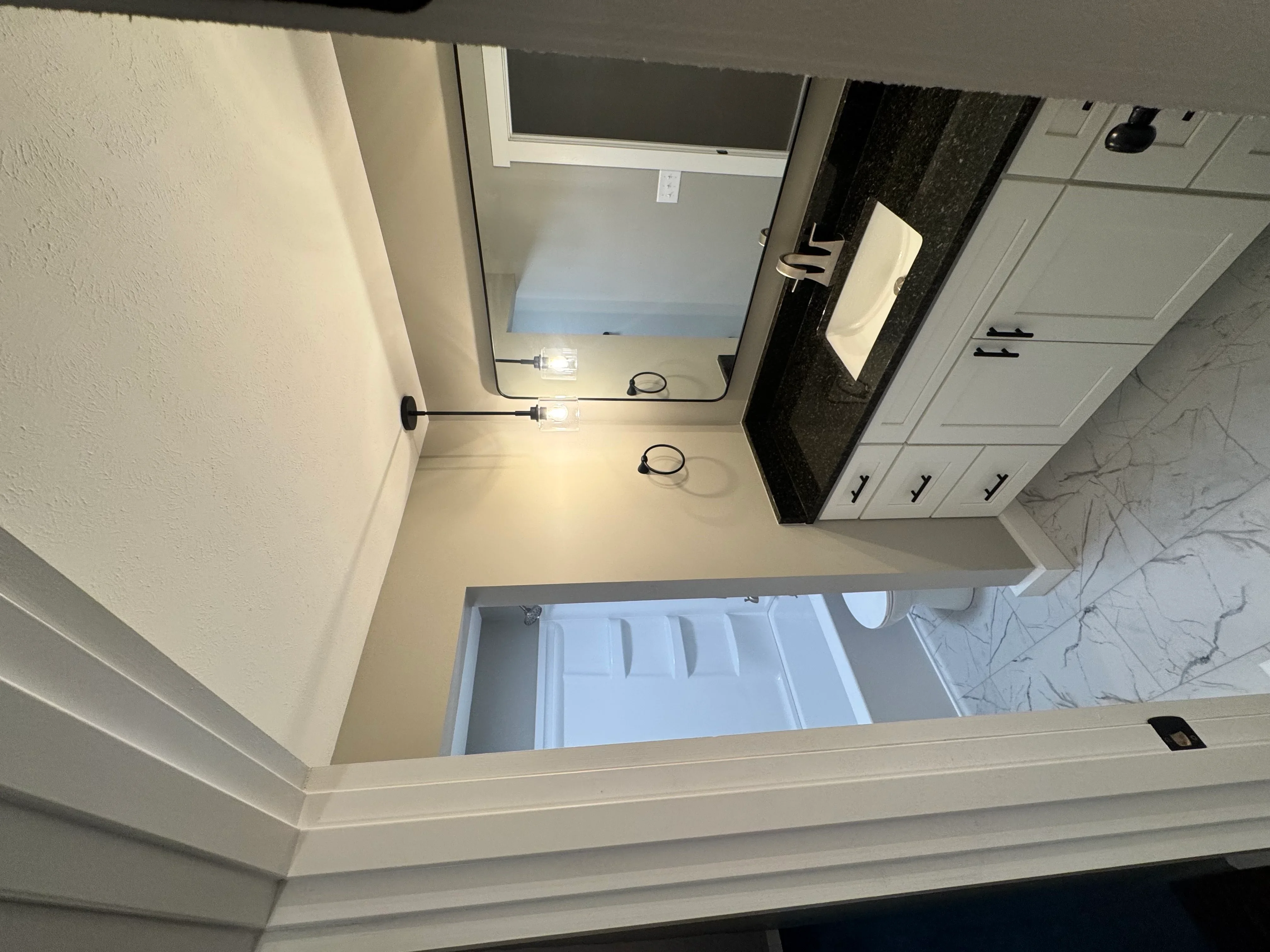 Newly installed bathroom vanity with white cabinets, black countertop, and marble tile flooring